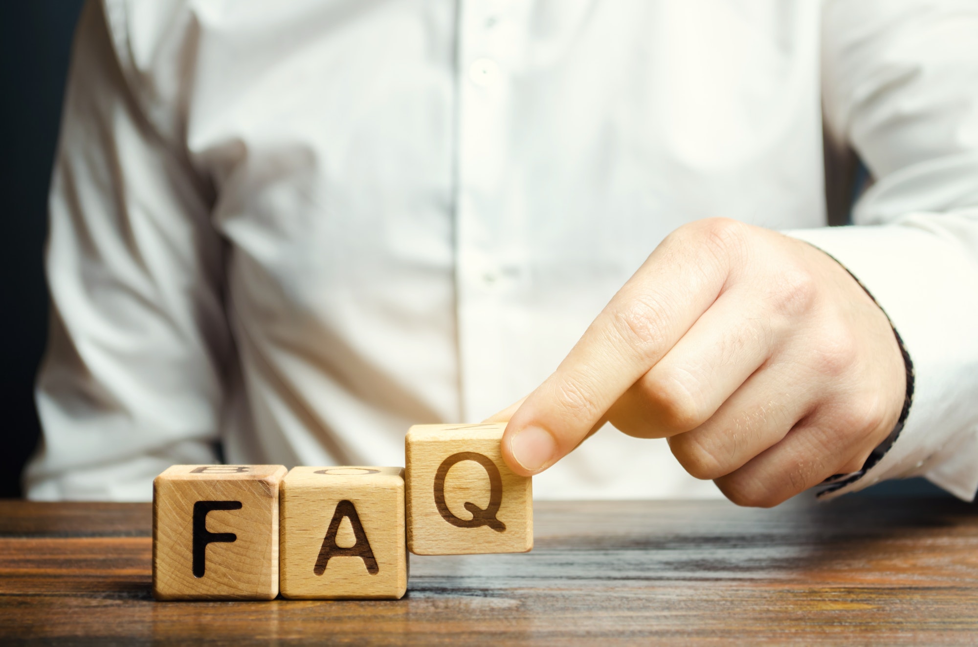 Businessman puts wooden blocks with the word FAQ (frequently asked questions)